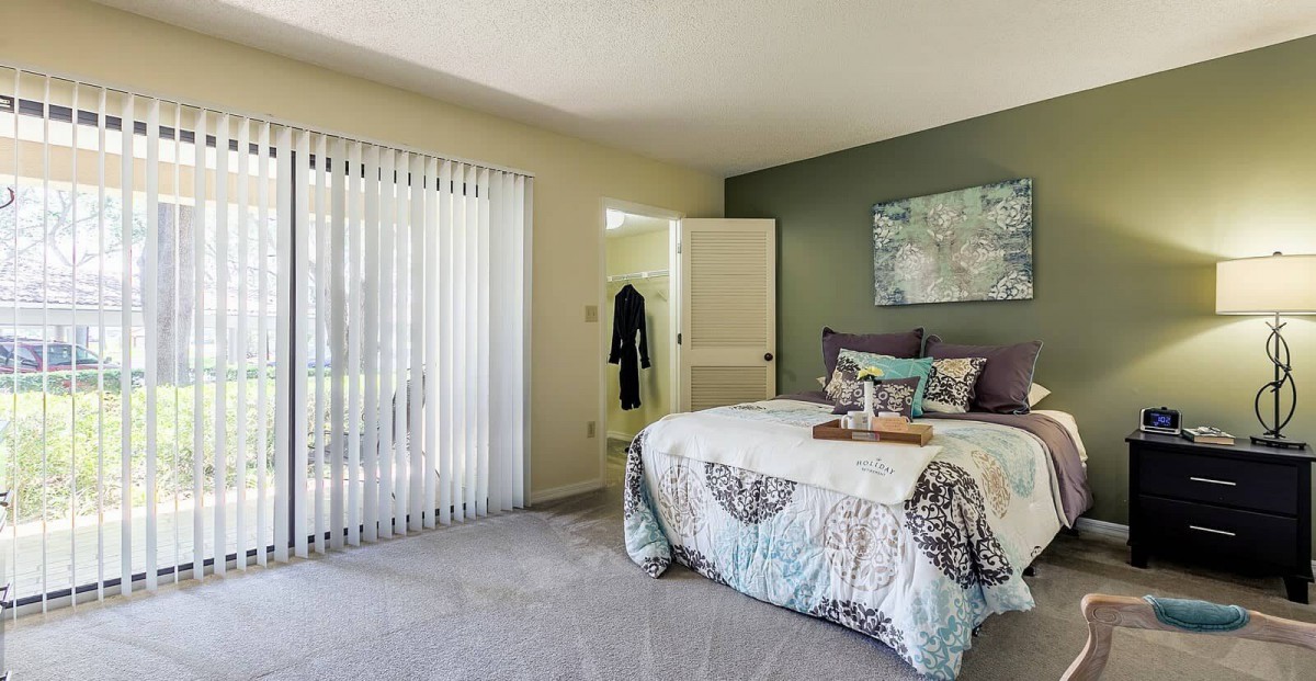 A cozy bedroom featuring a neatly made bed with decorative pillows, soft lighting, and a sliding glass door.
