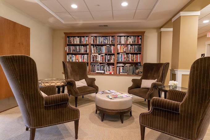 A cozy reading room with four chairs arranged around a small table, surrounded by a large bookshelf filled with books.