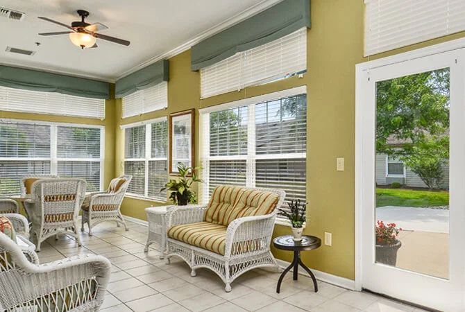 A bright sunroom with wicker furniture, large windows, and indoor plants.