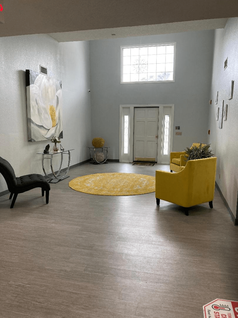 A modern living room with gray walls, featuring yellow accents, a round rug, and stylish artwork.