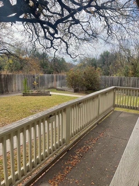 A backyard with a wooden deck, surrounded by a fence, featuring grass and garden beds.
