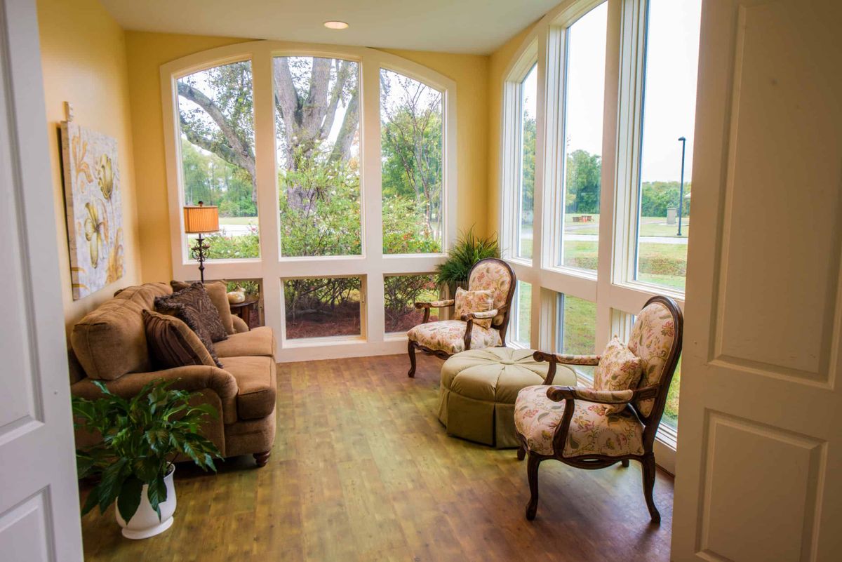 A cozy sunroom with large windows, filled with natural light and furnished with elegant chairs and a sofa.