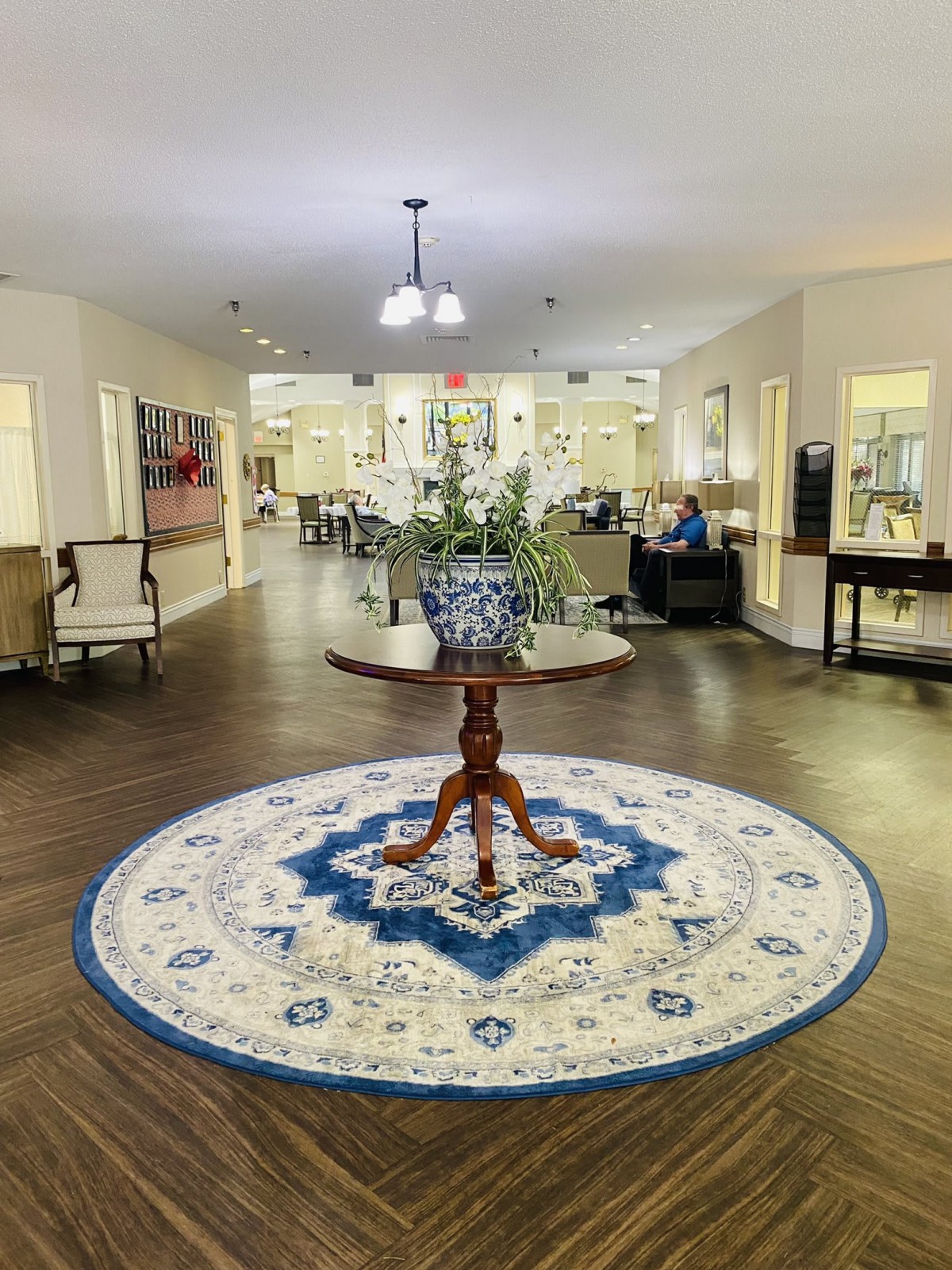 A welcoming lobby featuring a central round wooden table with a vase of flowers on an ornate circular rug.