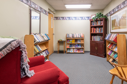 A cozy reading nook featuring shelves filled with books, a red sofa, and warm lighting.