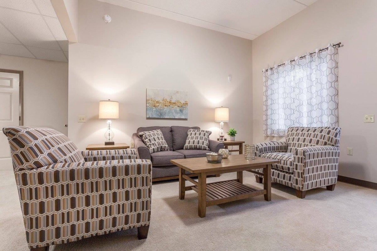 A cozy living room with sofas, armchairs, a wooden coffee table, and warm lighting.