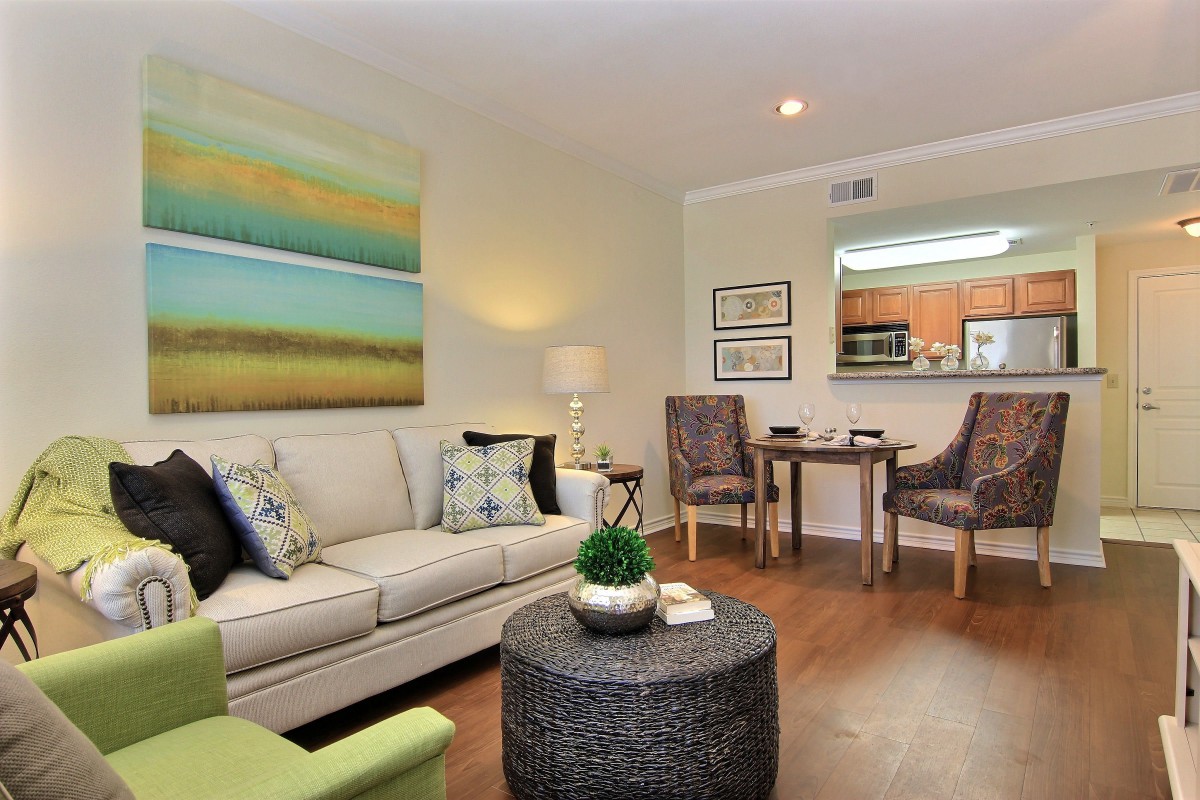 A cozy living room with modern decor, featuring a sofa, art on the wall, a lamp, and a small dining area.