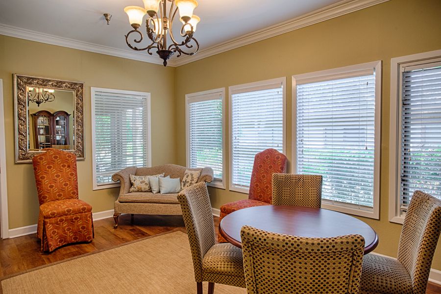 A cozy dining room with a round table, chairs, and a couch by the windows.