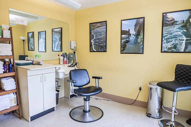 A well-lit salon with a single barber chair, mirror, and yellow walls adorned with posters.