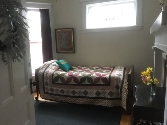 A cozy bedroom with a patterned quilt on the bed and artwork on the wall.