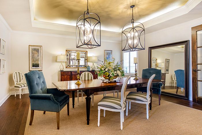 An elegant dining room featuring a wooden table, upholstered chairs, and stylish chandeliers.