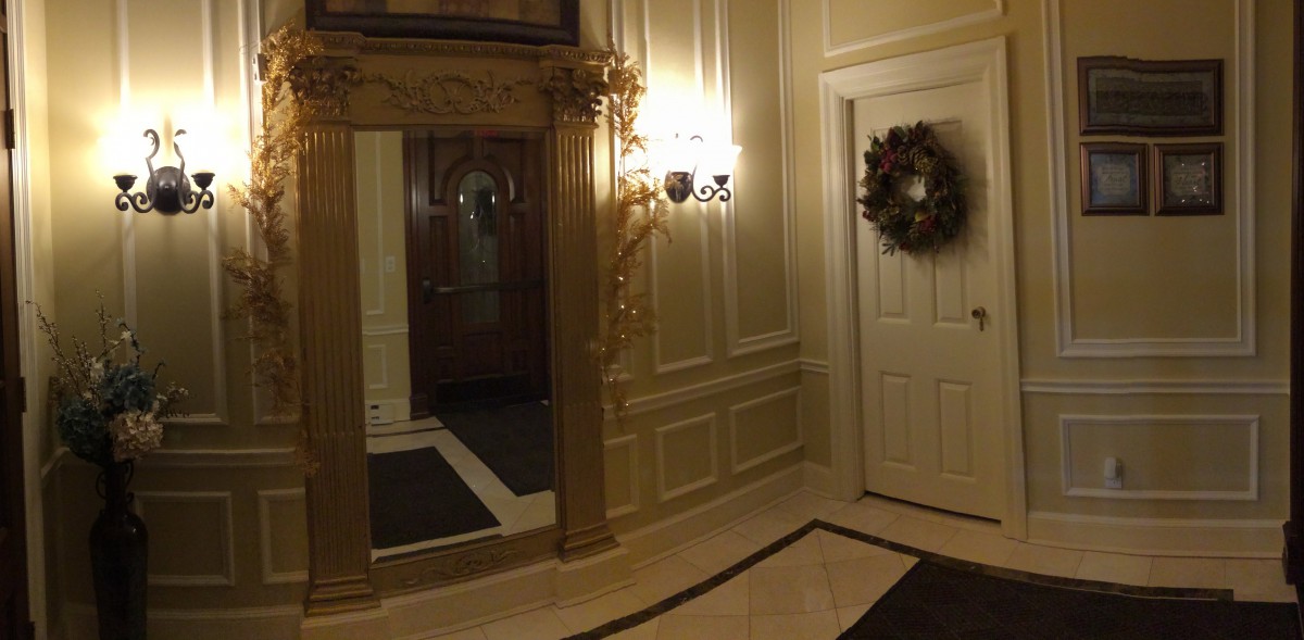 An elegant hallway featuring a large mirror, decorative lighting, and a door adorned with a wreath.