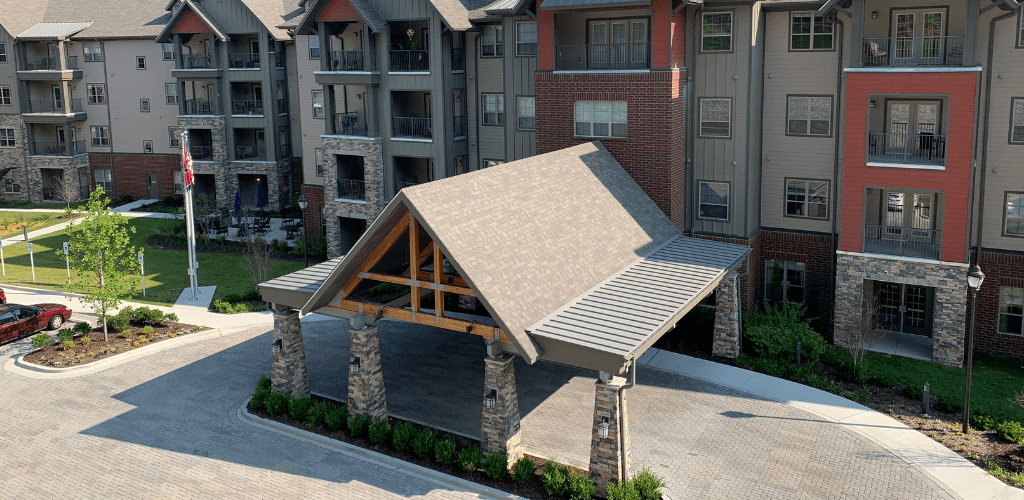 A modern apartment complex with a covered entrance featuring stone pillars and a pitched roof.