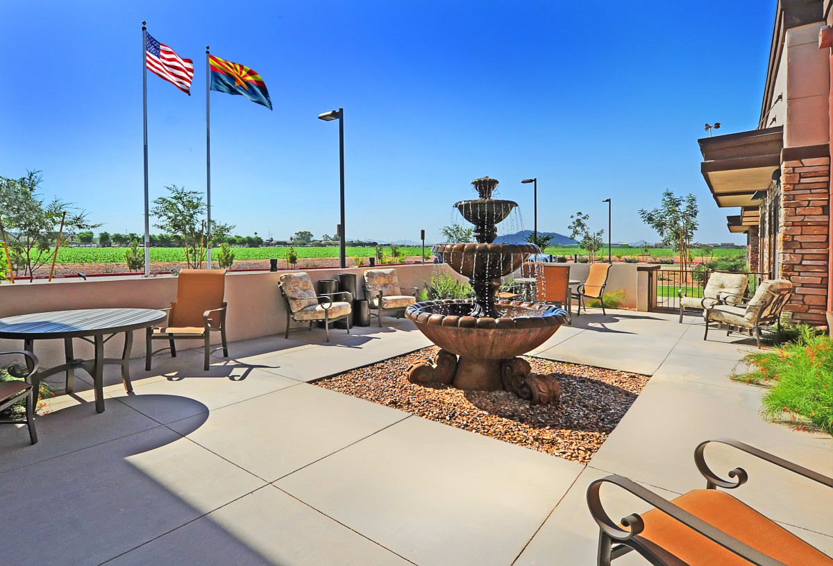 A scenic patio with a fountain, outdoor seating, and flags against a clear blue sky.
