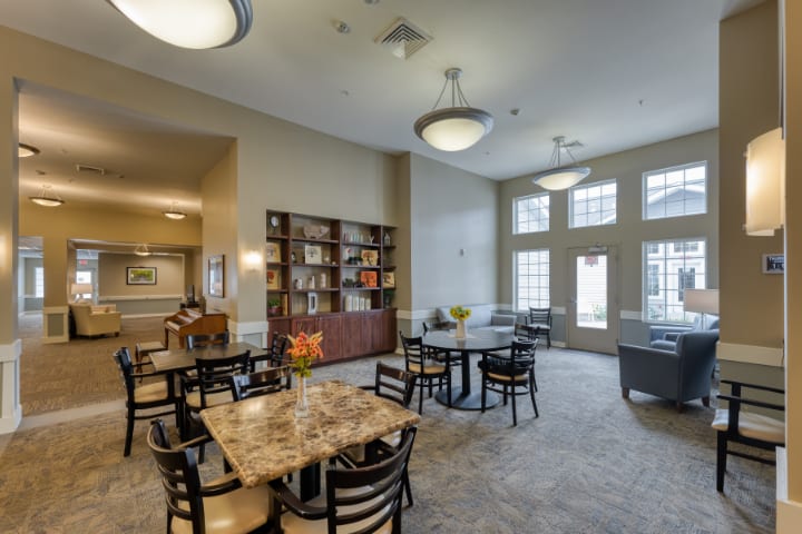 A well-lit dining area with multiple tables and chairs, featuring a bookshelf and decorative elements.