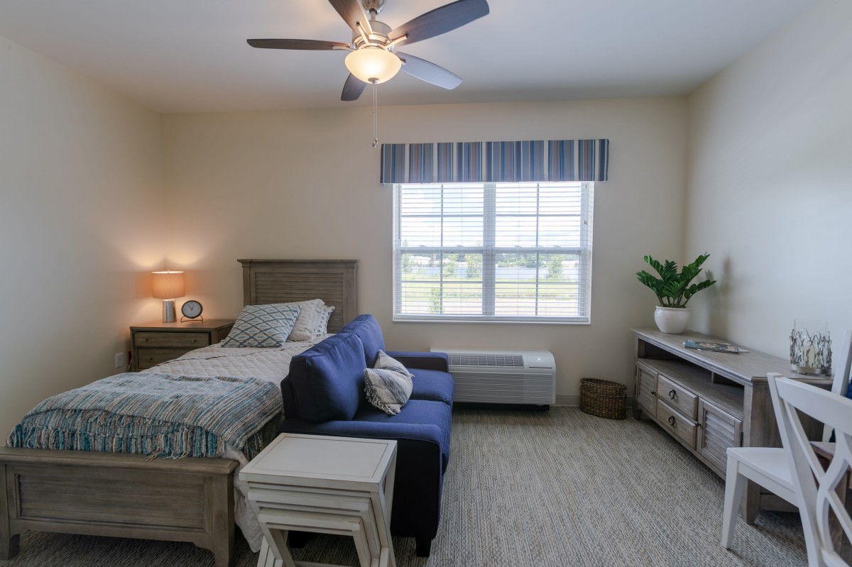 A cozy bedroom featuring a bed, sofa, and ample natural light from a large window.