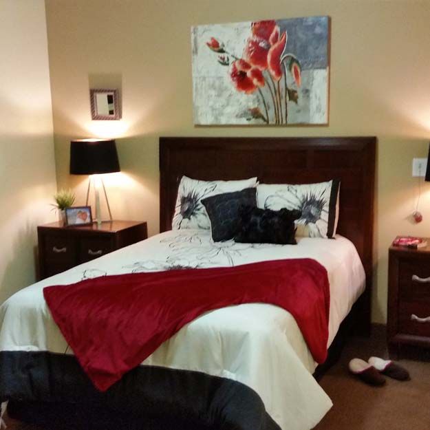 A cozy bedroom with a neatly made bed, flanked by two nightstands and stylish lamps, adorned with a red throw blanket and floral artwork above the headboard.