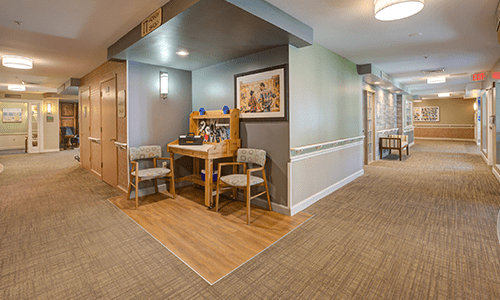 A cozy hallway nook featuring a wooden desk, two chairs, artwork on the wall, and soft lighting.