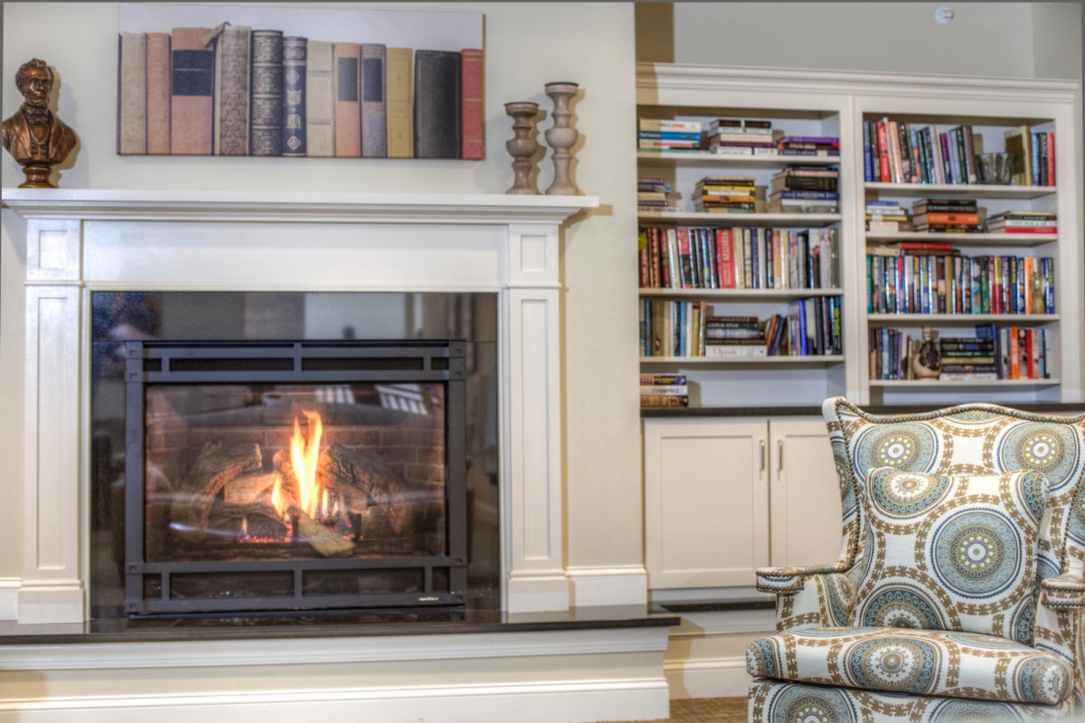A cozy living room with a lit fireplace and a well-stocked bookshelf.