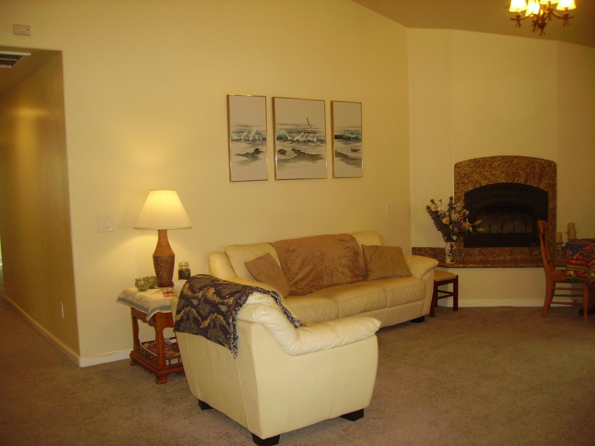 A cozy living room with a cream-colored sofa, a lamp on a side table, artwork on the wall, and a fireplace in the corner.