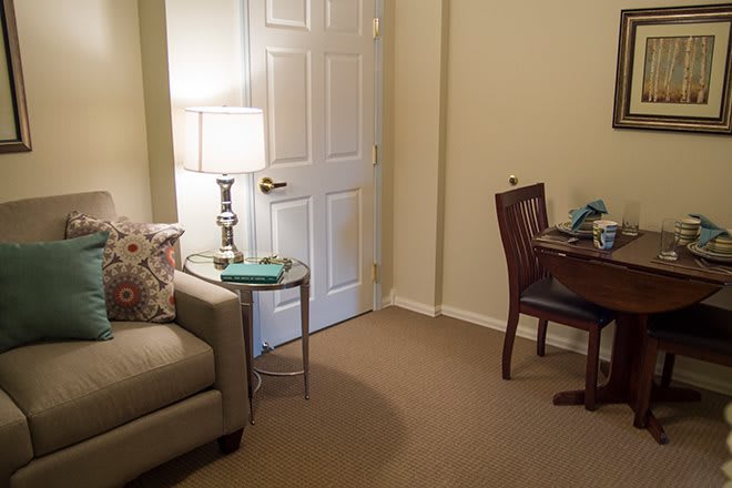 A cozy living room setup featuring a sofa, a lamp on a side table, and a small desk with a chair.