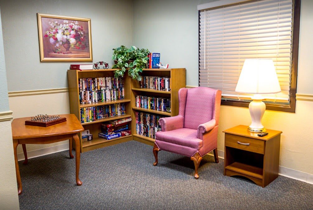 A cozy reading corner with a pink armchair, surrounded by bookshelves and a warm lamp.