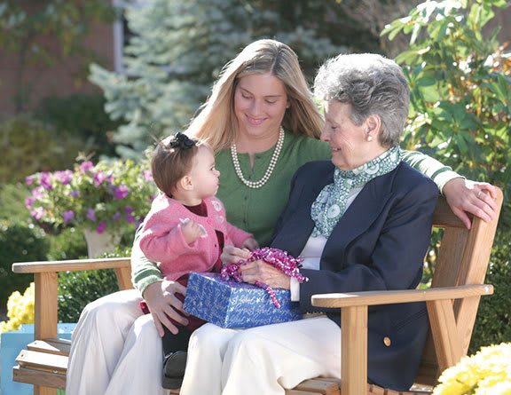 A young woman, a child, and an elderly woman sitting together on a bench in a garden.