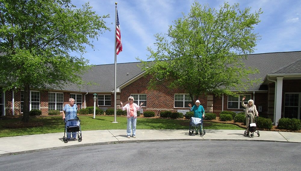 Three seniors with walking aids standing outside a building on a sunny day, with an American flag in the background.