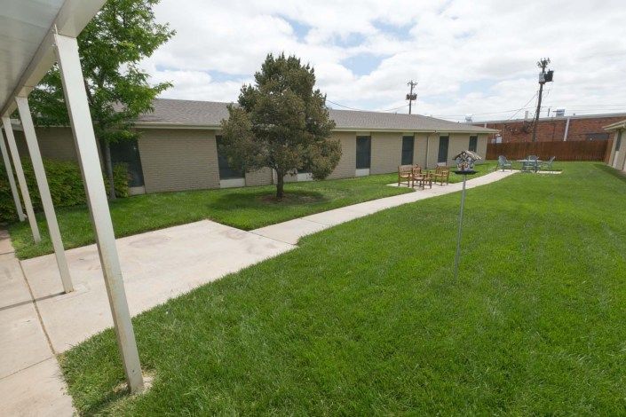 A single-story building surrounded by a well-maintained lawn and a paved sidewalk under a cloudy sky.