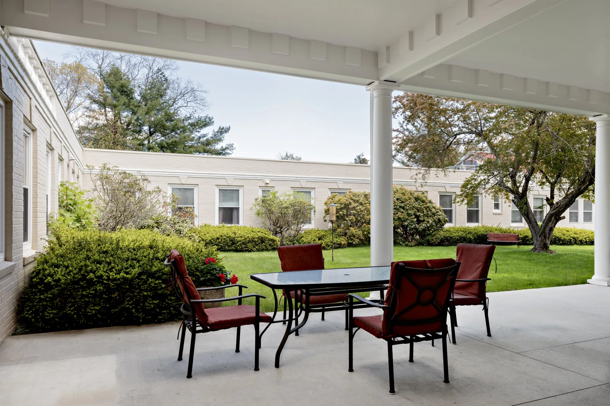 A serene outdoor patio with a table and chairs, surrounded by lush greenery.