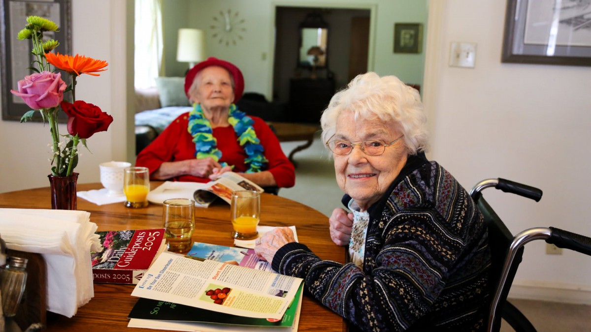 Two elderly women enjoying a conversation at a table with magazines and drinks.