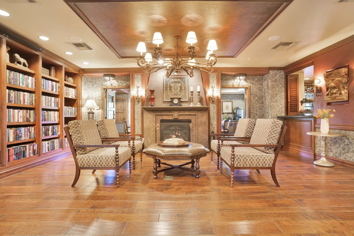 A luxurious living room with a central fireplace, elegant chairs, and a chandelier.