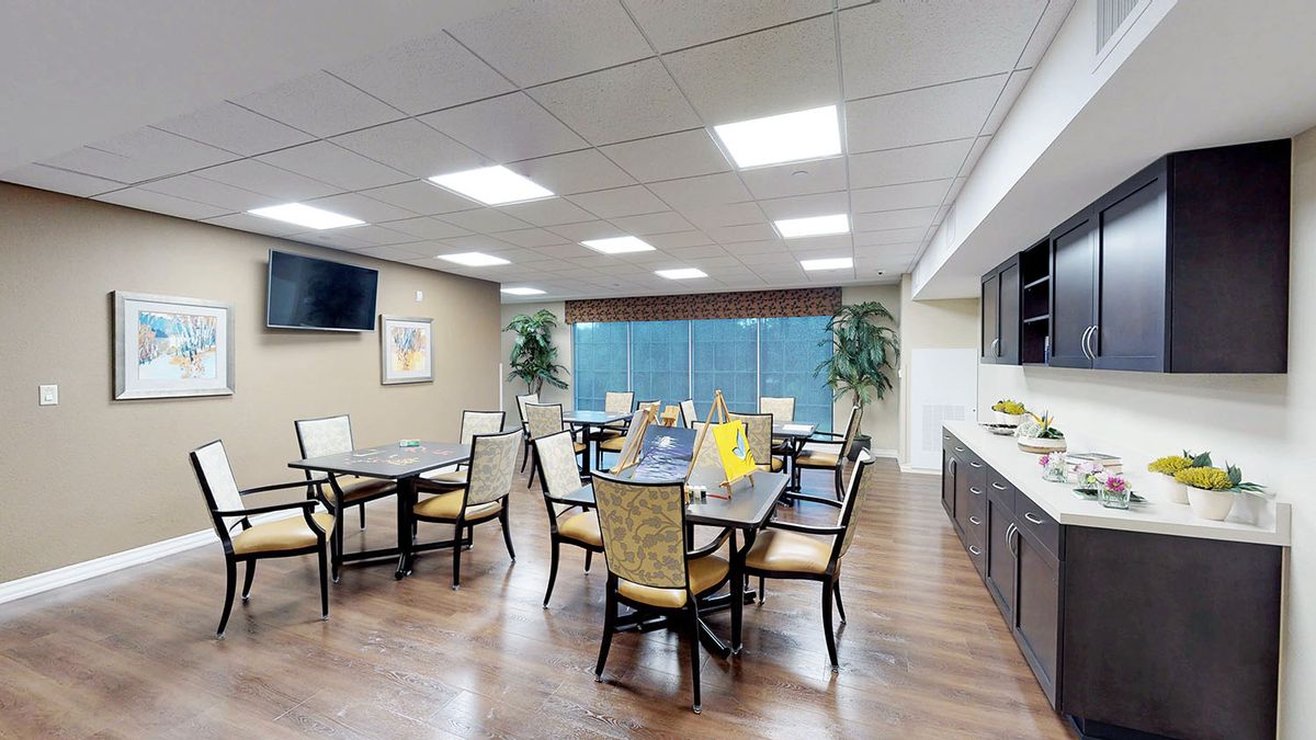 A spacious dining area with multiple tables and chairs, featuring large windows and a television on the wall.