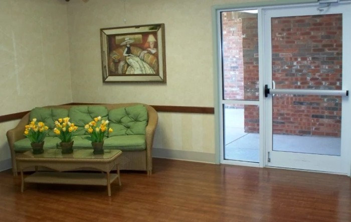 A cozy waiting room with a green sofa, wooden table adorned with flowers, and a painting on the wall.