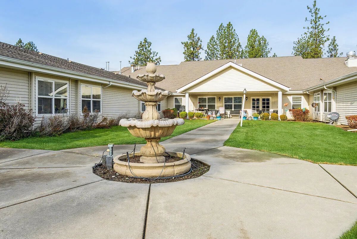 A scenic courtyard featuring a tiered fountain in front of a residence surrounded by greenery.
