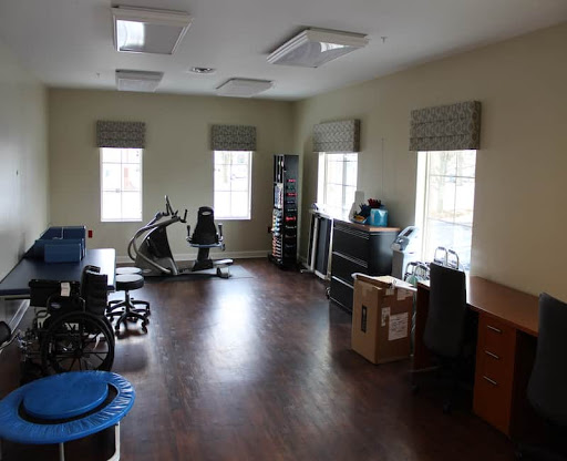 A spacious, empty room featuring office and exercise equipment with ample natural light from large windows.