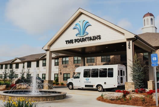 Entrance of 'The Fountains' featuring a parked shuttle van and a decorative fountain.