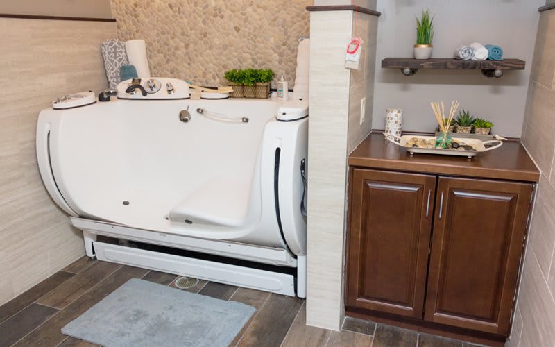 A bathroom featuring a walk-in bathtub alongside a wooden cabinet and sink.